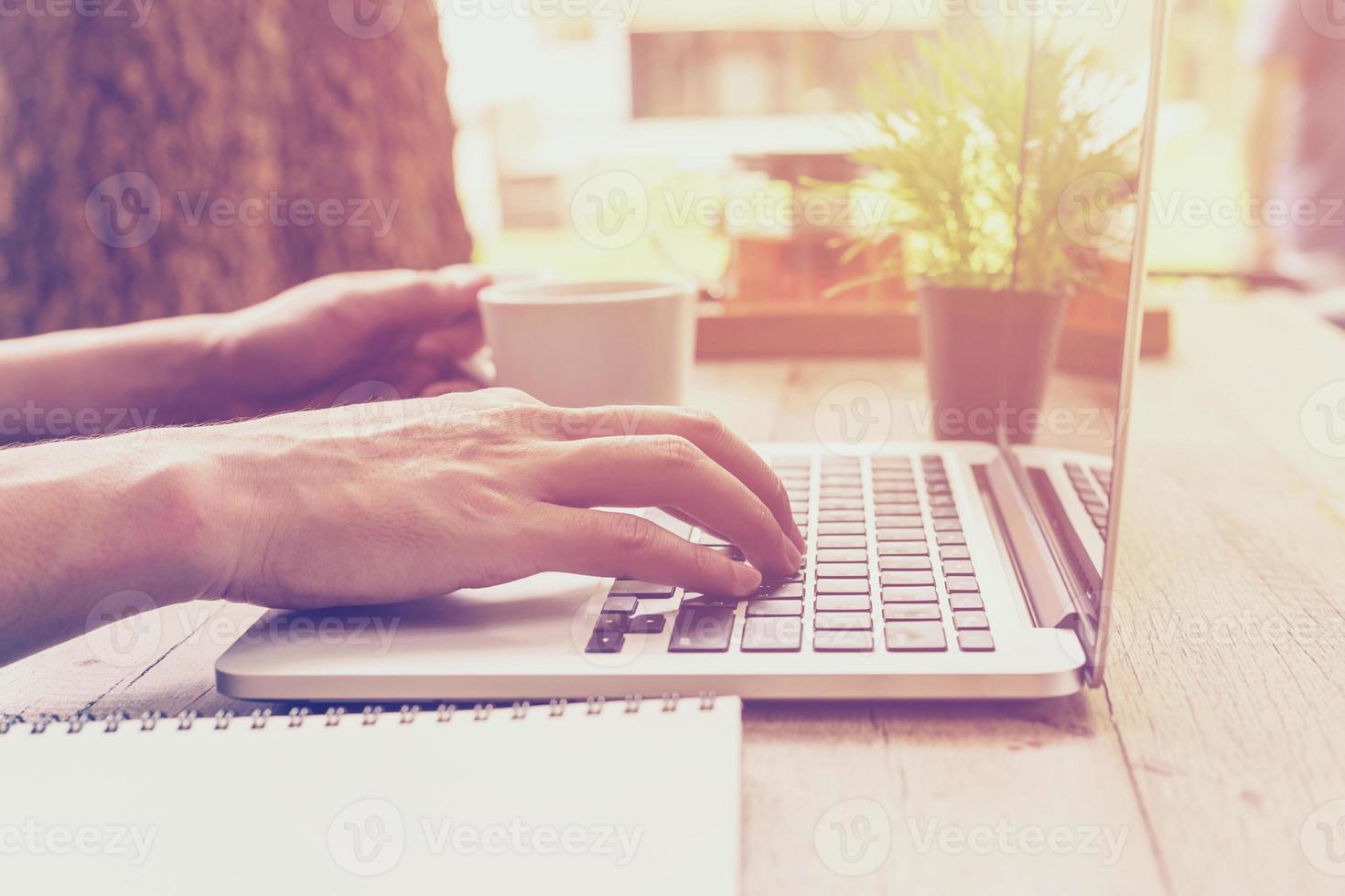 fechar acima mão o negócio homem segurando copo café e usando computador portátil dentro café fazer compras com vintage tonificado. foto