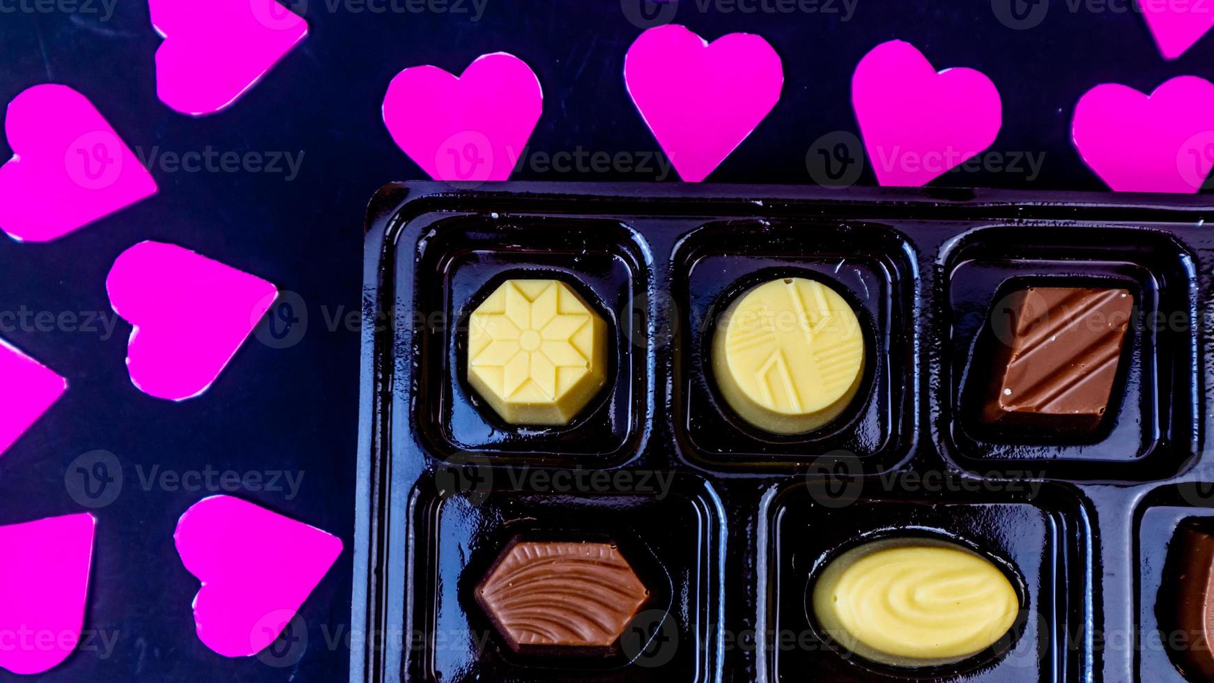 delicioso chocolate rodeado por corações rosa em fundo preto foto