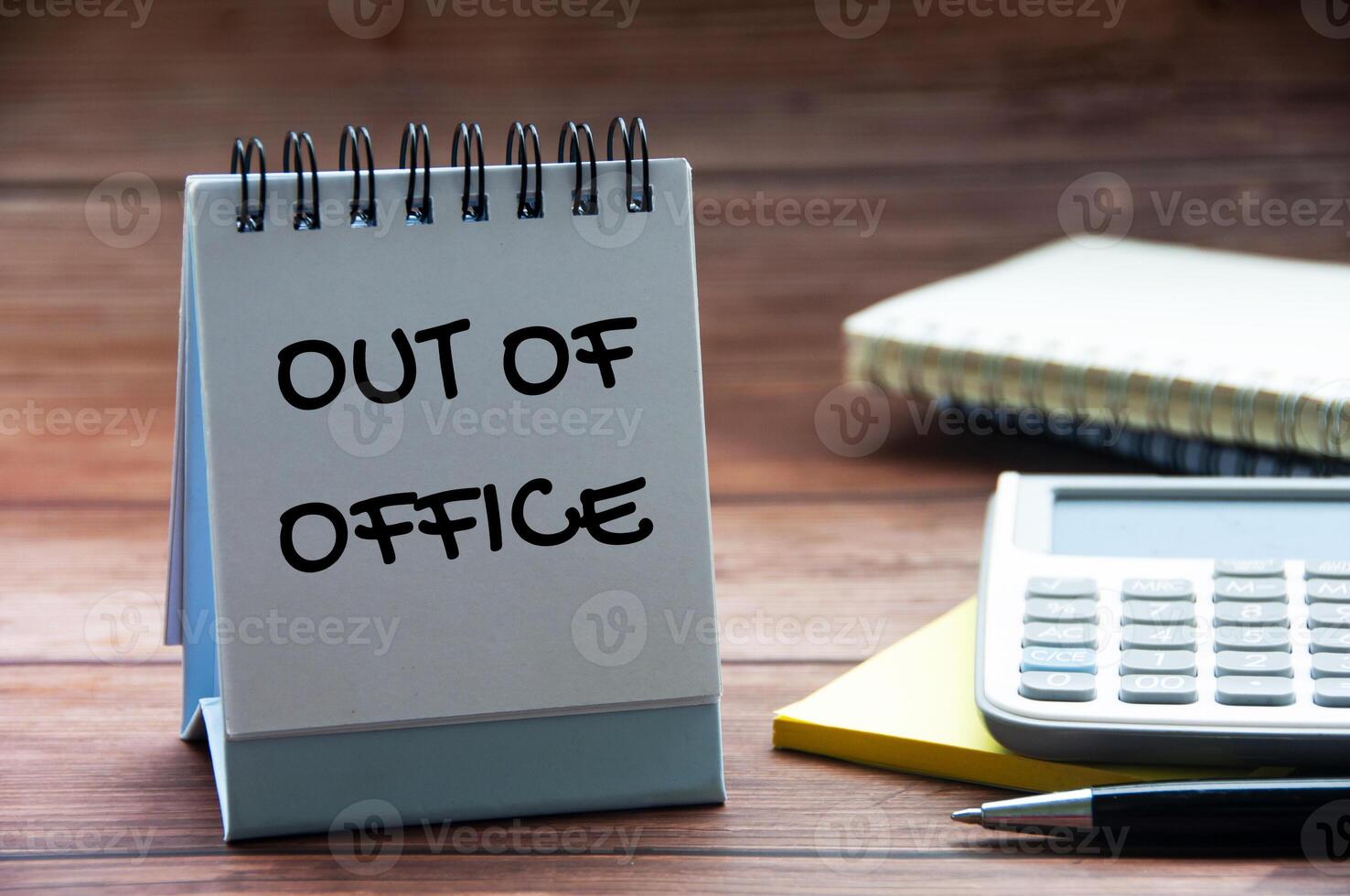 Fora do escritório texto em calendário escrivaninha com caderno, calculadora e caneta fundo. Fora do escritório conceito. foto