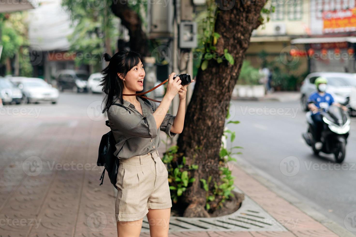 jovem ásia mulher mochila viajante usando digital compactar Câmera, desfrutando rua cultural local Lugar, colocar e sorriso. foto
