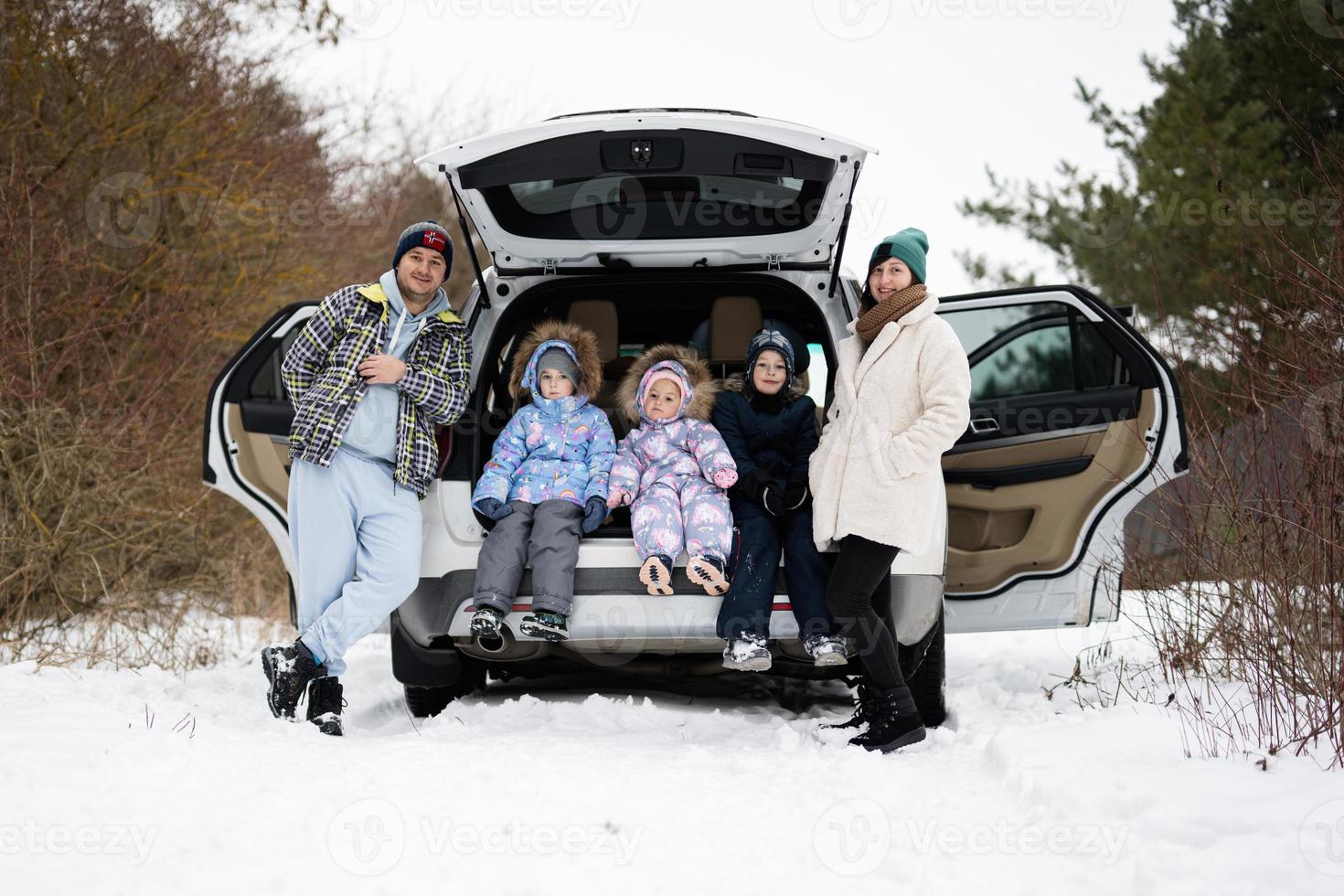 família com crianças sentar em carro suv com aberto tronco ficar de pé dentro inverno floresta. foto