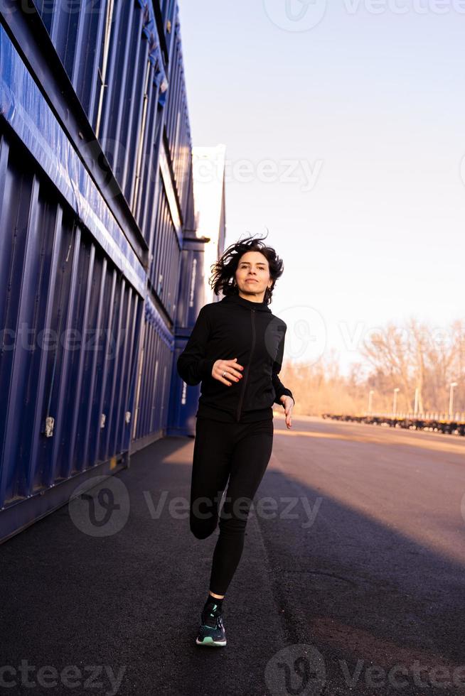 jovem adulto mulher é corrida dentro a manhã entre a Remessa containers do uma comercial porta foto