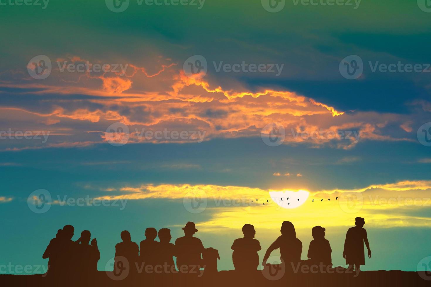 silhueta pessoas sentado em a chão e nascer do sol em a colorida céu laranja nuvem e pássaros vôo foto