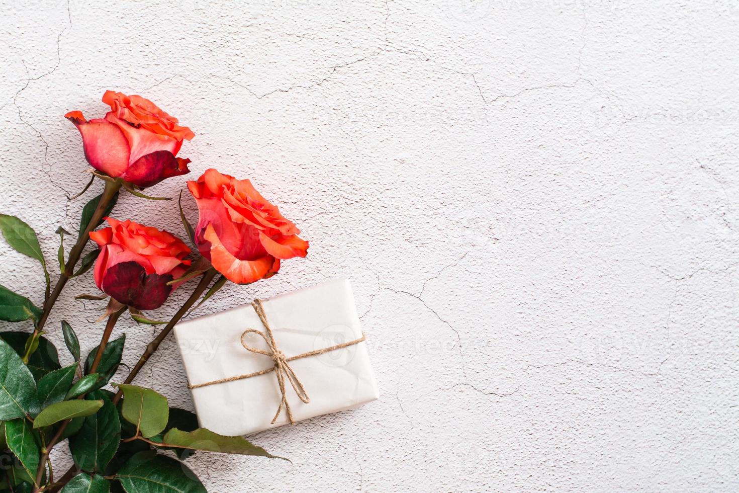 fresco vermelho rosas e uma caixa dentro construir papel em uma texturizado cinzento fundo. feriado presente, Parabéns. topo visualizar. foto