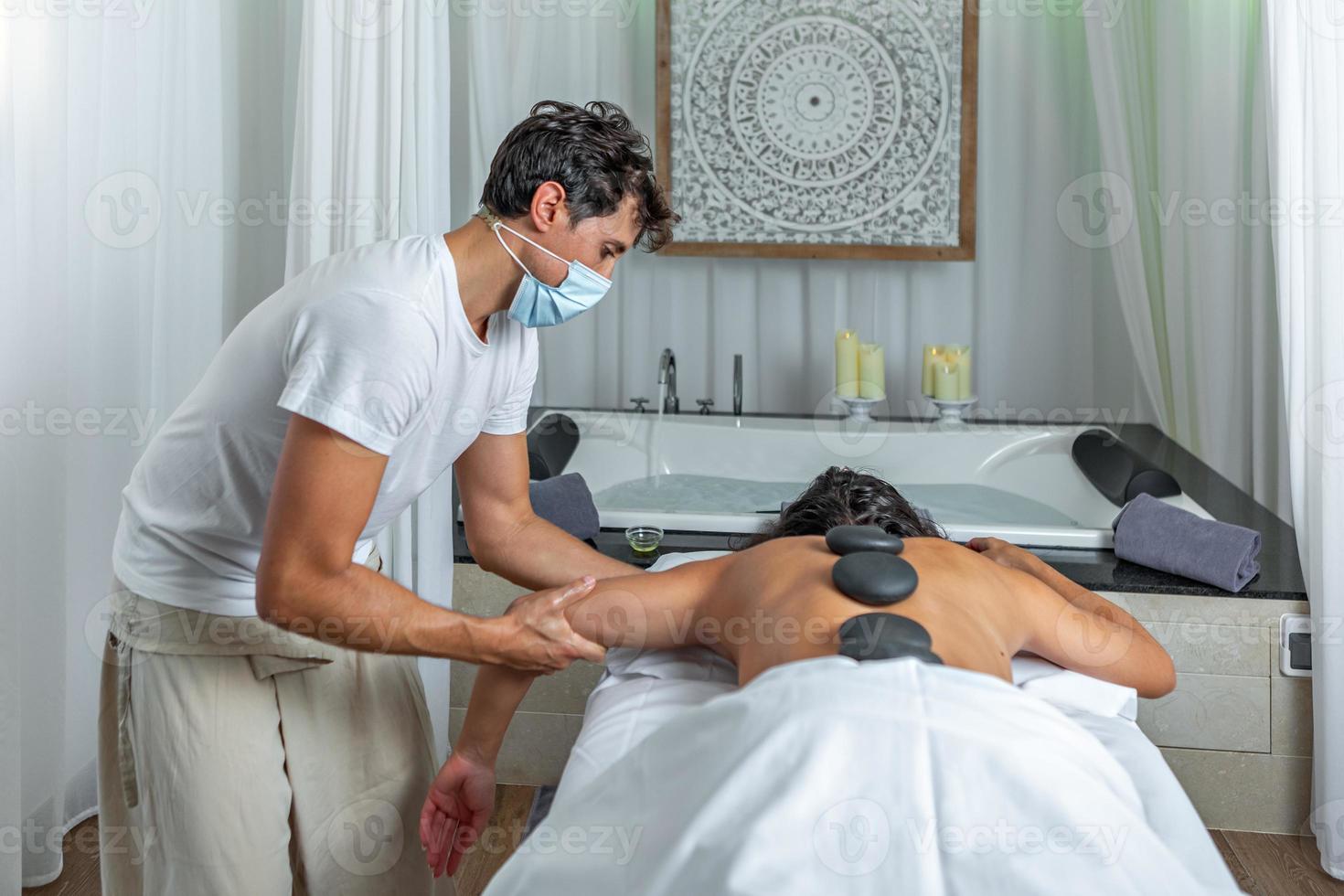traseiro Visão do uma massagista dando a braço massagem para a adulto mulher com quente pedras dentro dela costas para massagem costas tratamento dentro spa salão foto