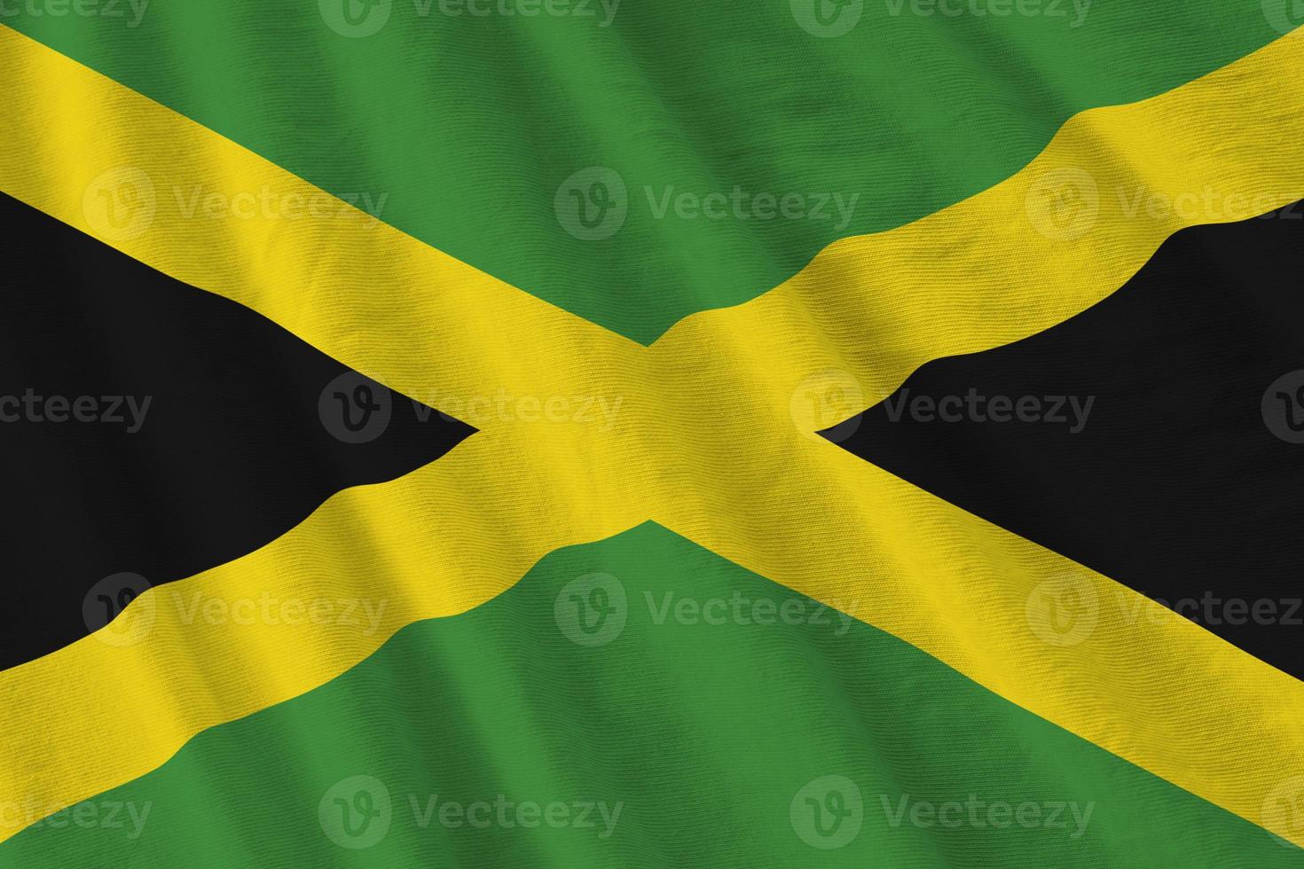 bandeira da jamaica com grandes dobras acenando de perto sob a luz do estúdio dentro de casa. os símbolos oficiais e cores no banner foto