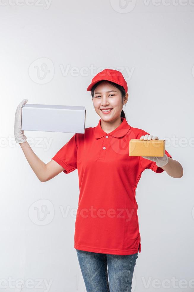 imagem do jovem entregador em uniforme de camiseta em branco de boné vermelho em pé com caixa de papelão branca vazia isolada no estúdio de fundo cinza claro foto