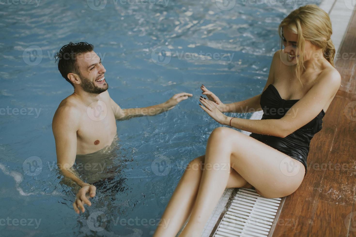 jovem casal relaxando à beira da piscina interior foto