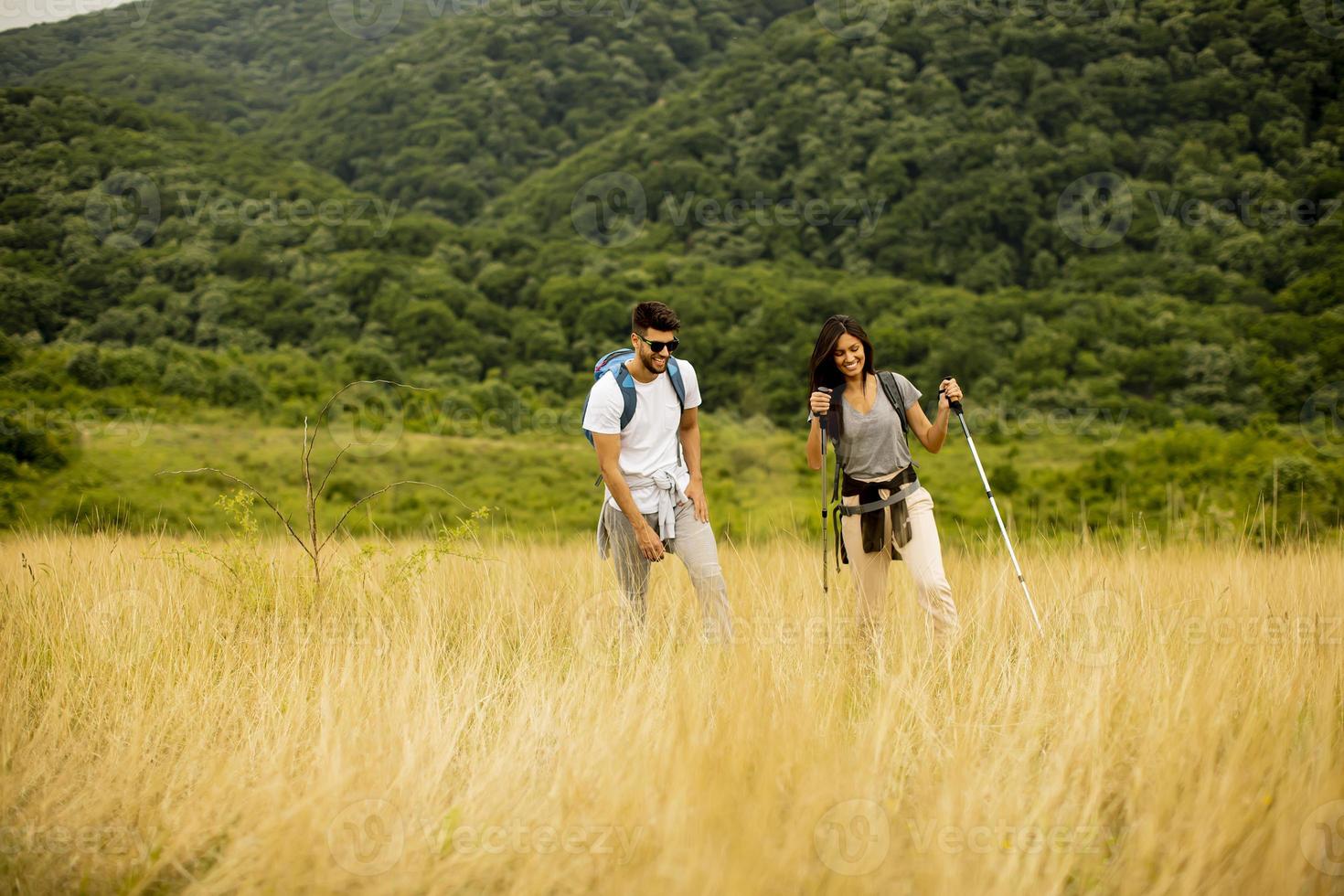 casal sorridente caminhando com mochilas pelas colinas verdes foto