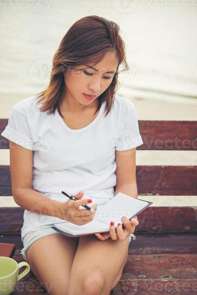 bela jovem escrevendo no bloco de notas enquanto está sentado no banco foto