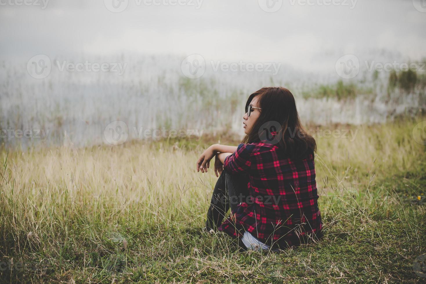 mulher jovem hippie sentada na grama perto de um lago foto