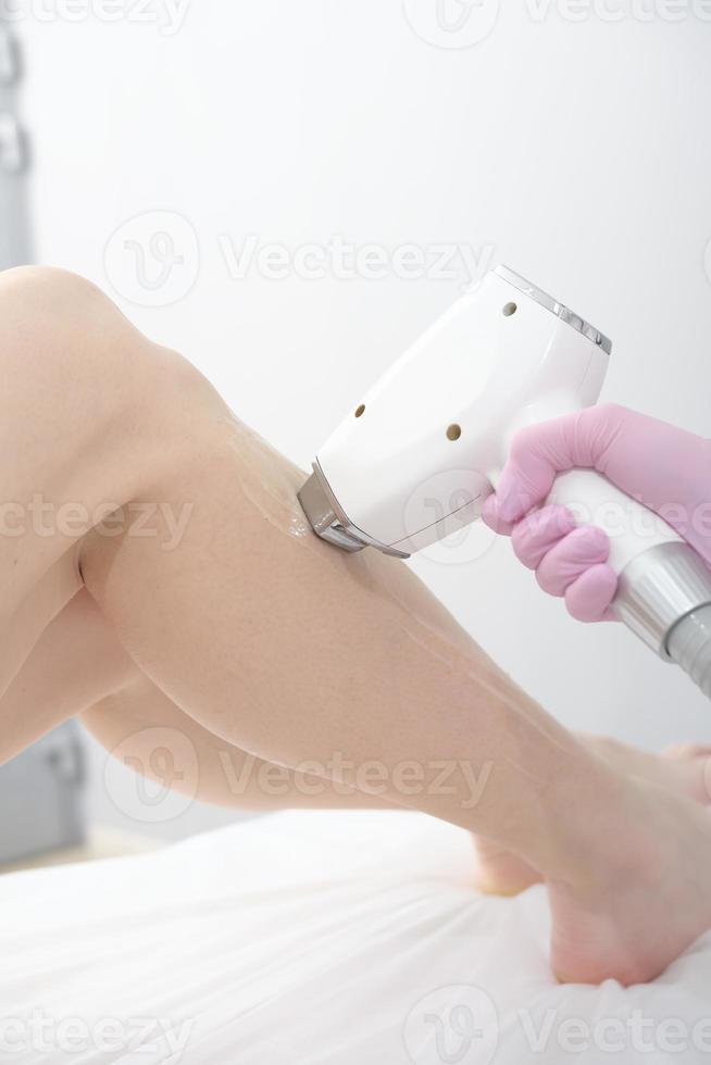 laser depilação procedimento, esteticista tocante mulher perna com laser aparelho. pele Cuidado, suave e lindo pernas dentro salão., vertical foto