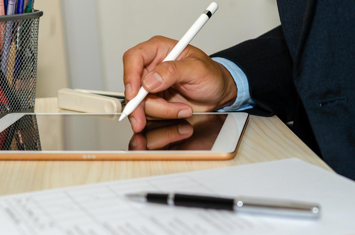 um empresário usando um tablet com documentos de negócios e canetas na mesa foto