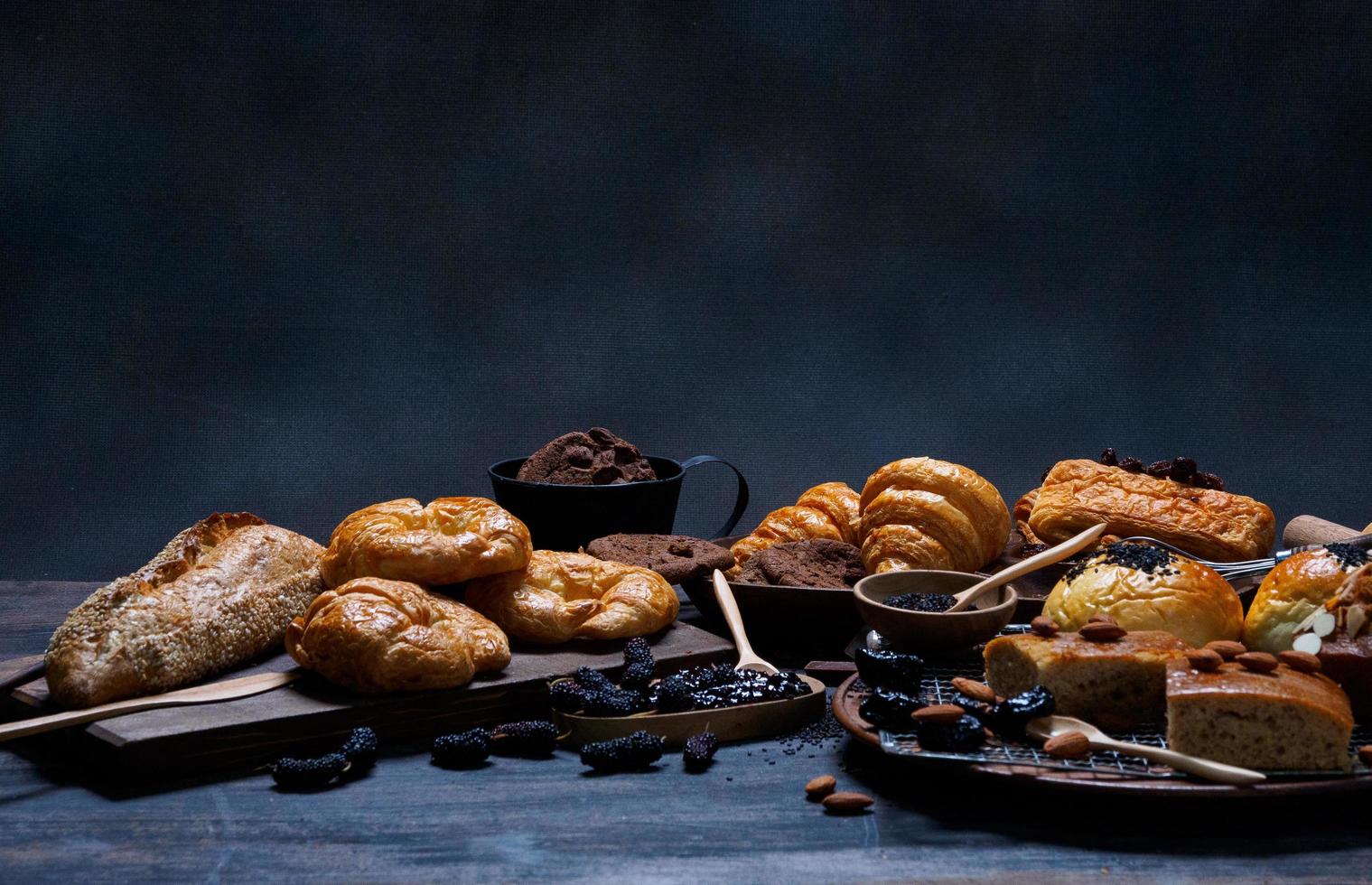 vista superior pão fresco passas marrom gergelim padaria feita de farinha de trigo comida caseira adequada para uma alimentação saudável no chão de mesa de madeira preto rústico fundo escuro foto