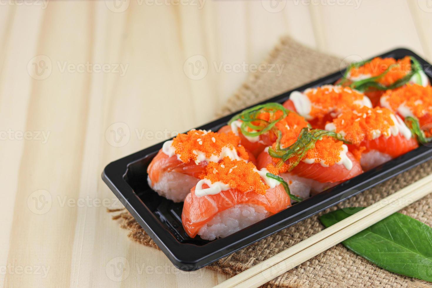 Sushi de salmão na placa preta e tapete de aniagem com pauzinhos na mesa de madeira foto