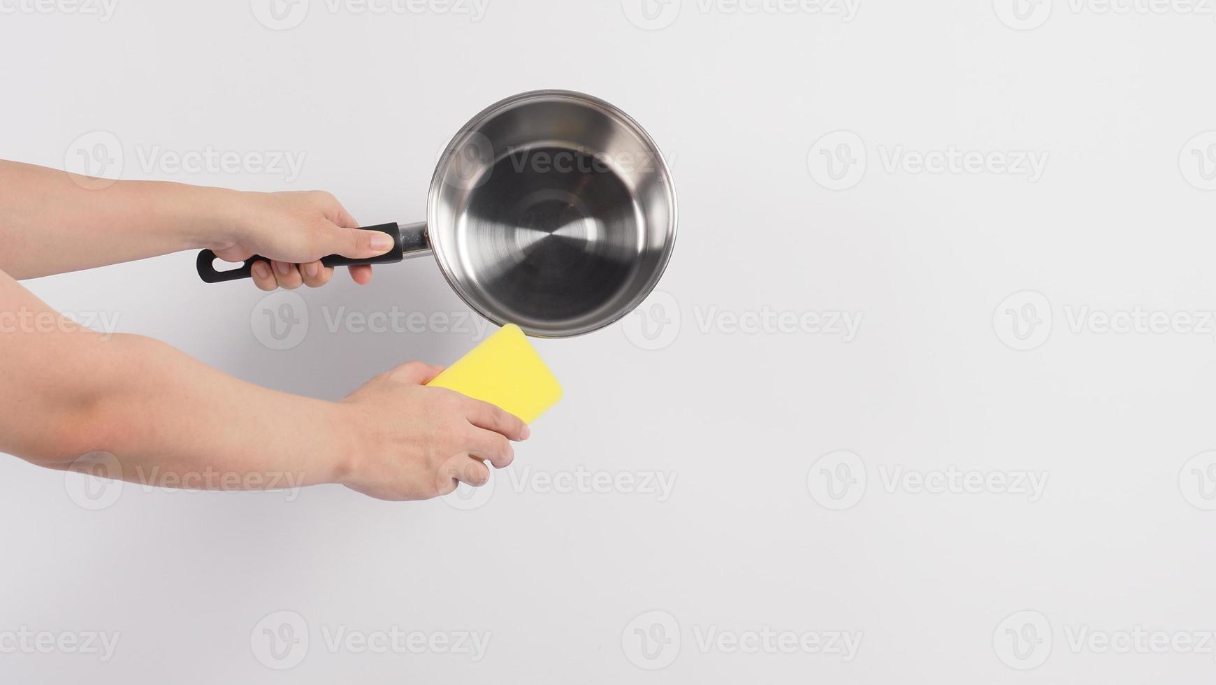 mão de homem de limpeza de pote em fundo branco limpando o pote antiaderente com esponja de lavar louça prática que cor amarela no lado macio e verde no lado duro para higiene após o cozimento. panela elétrica foto