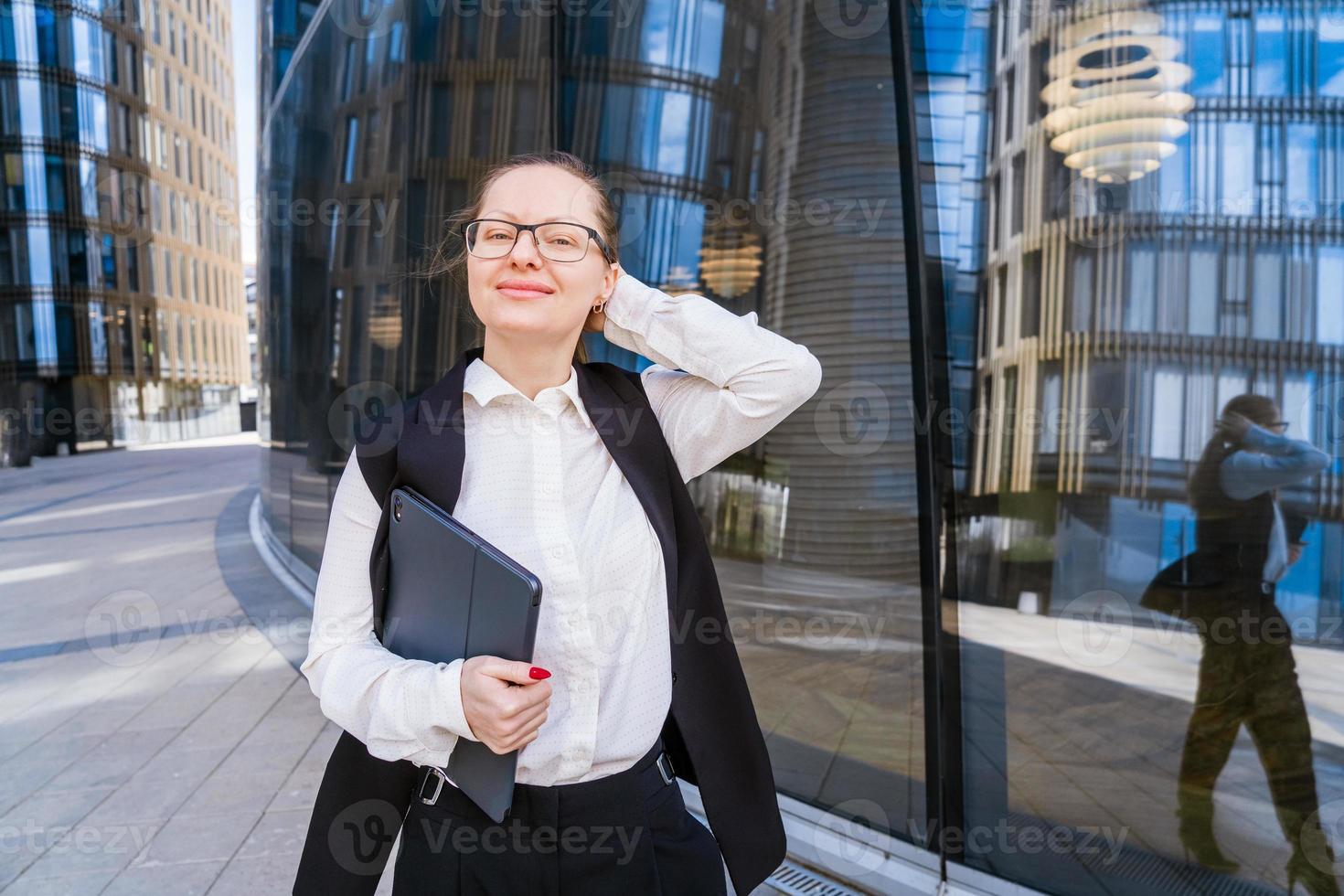 o negócio caucasiano mulher segurando uma computador portátil e ao ar livre cercado de edifícios. foto