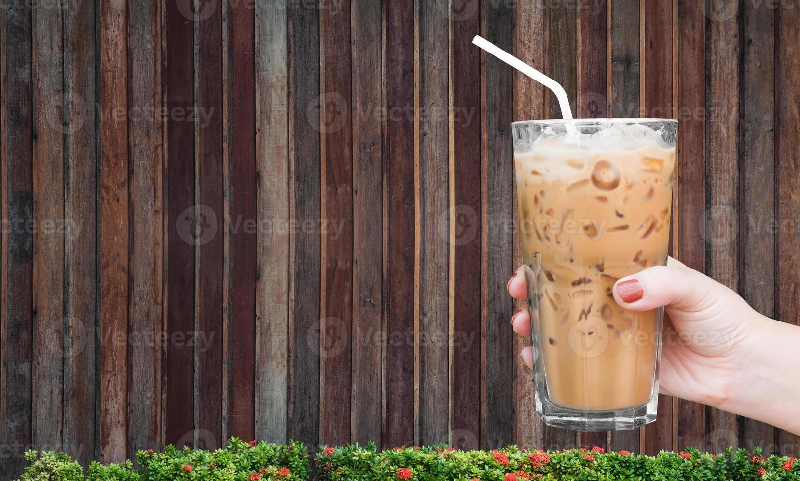 mulher mão segurando a vidro gelado café em de madeira fundo, gelado café com leite café foto