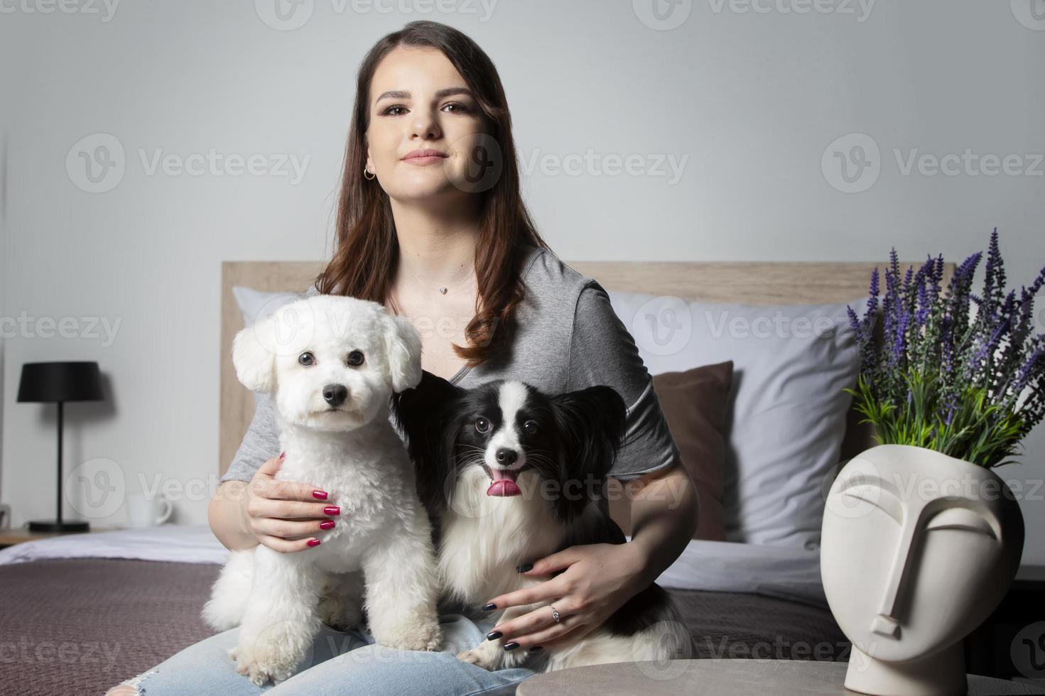 lindo menina às casa com uma cachorro. uma anfitriã com uma bichon e uma papillon senta em a cama. foto