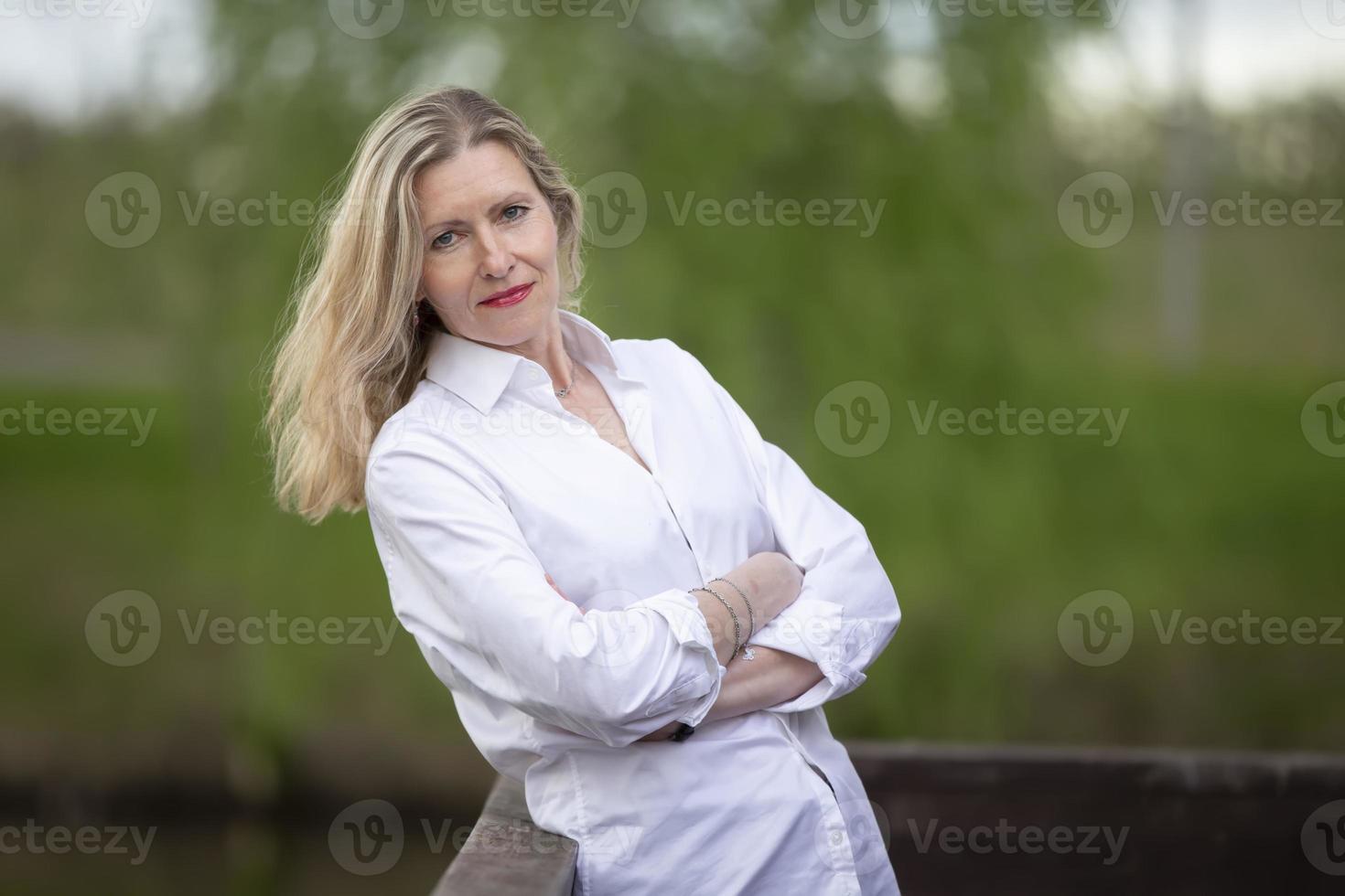 uma lindo meia idade europeu mulher. cinquenta anos Loiras mulher dentro uma branco camisa em a fundo do natureza. foto