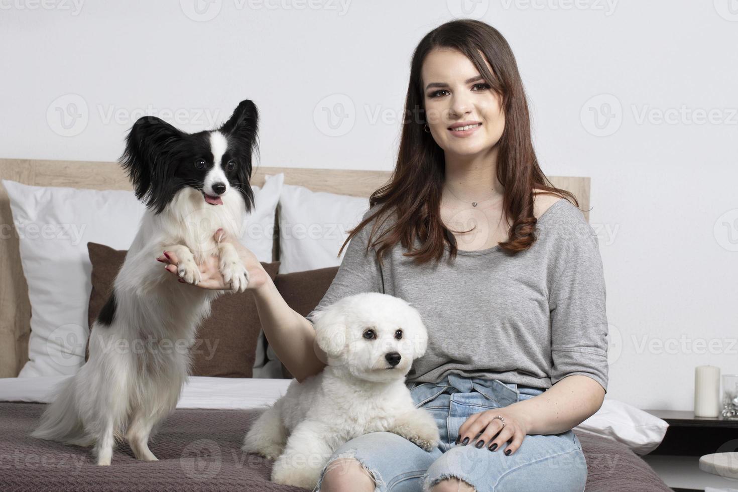 lindo menina às casa com uma cachorro. uma anfitriã com uma bichon e uma papillon senta em a cama. foto