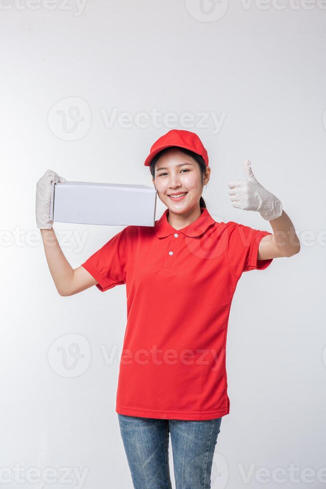 imagem do jovem entregador em uniforme de camiseta em branco de boné vermelho em pé com caixa de papelão branca vazia isolada no estúdio de fundo cinza claro foto