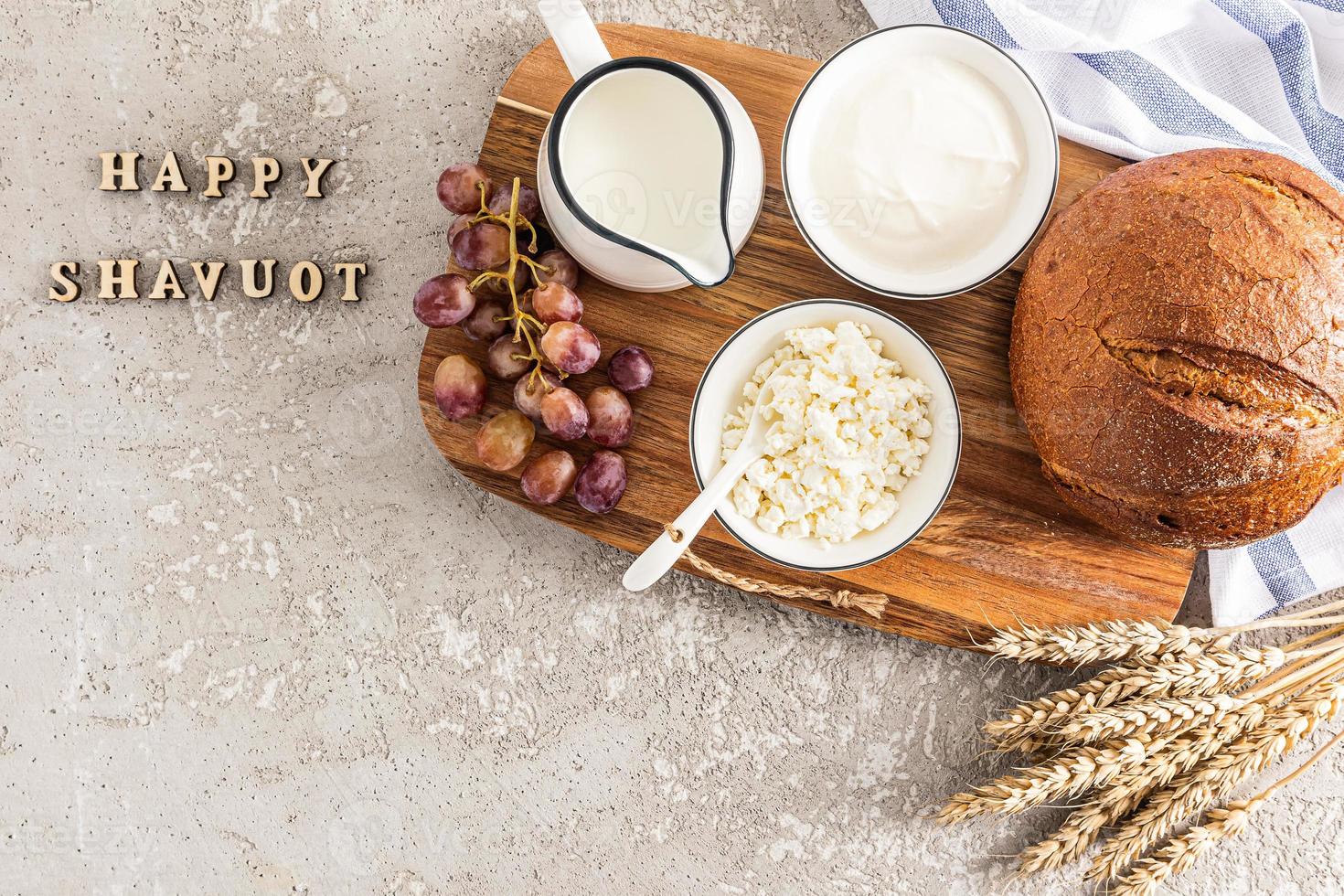 a Primavera feriado do a judeus do shavuot. uma festivo cartão com tradicional Comida e orelhas do milho. de madeira cartas em uma cinzento fundo - feliz shavuot. foto