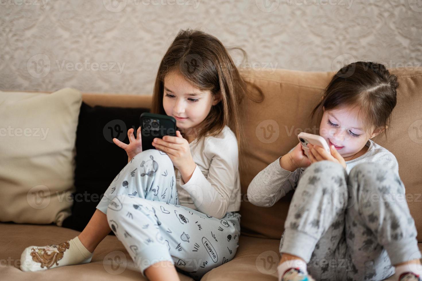 dois irmãs vestem pijamas jogando telefones cedo dentro manhã. foto