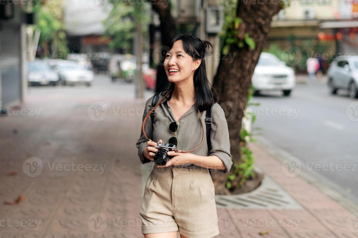 jovem ásia mulher mochila viajante usando digital compactar Câmera, desfrutando rua cultural local Lugar, colocar e sorriso. viajante verificação Fora lado ruas. foto