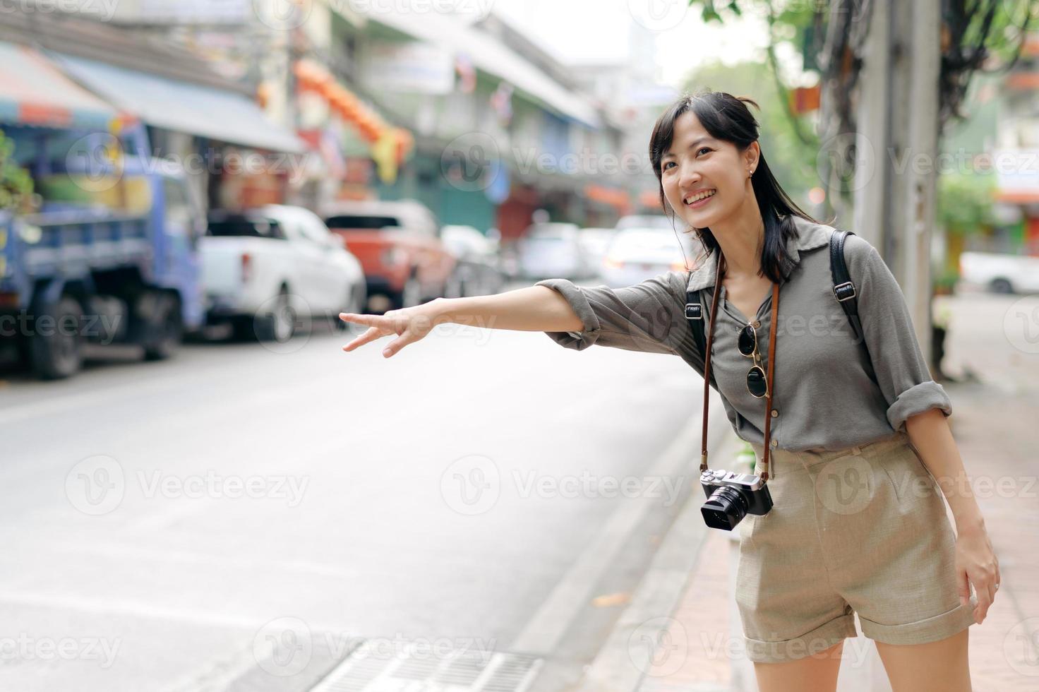 sorridente jovem ásia mulher viajante pedindo carona em uma estrada dentro a cidade. vida é uma viagem conceito. foto