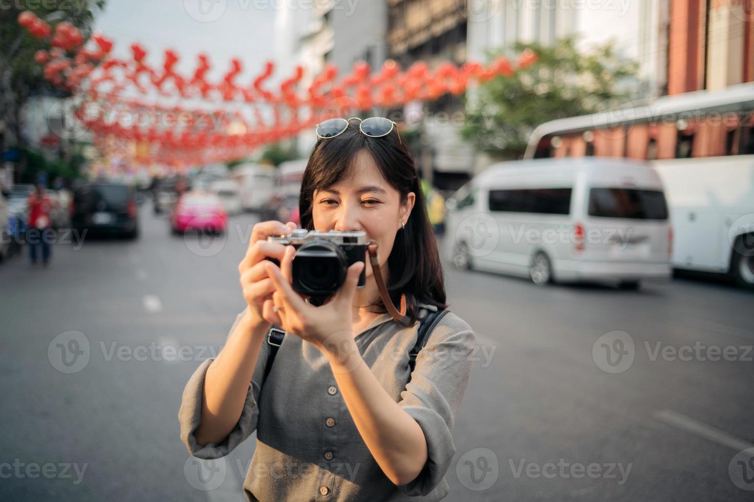 jovem ásia mulher mochila viajante usando digital compactar Câmera, desfrutando rua cultural local Lugar, colocar e sorriso. viajante verificação Fora lado ruas. foto