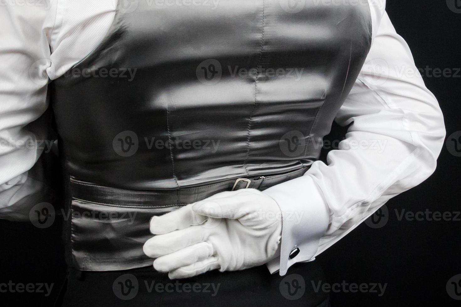 fechar acima do mordomo ou garçom vestindo colete com branco com luva mão atrás voltar. conceito do serviço indústria e elegante hospitalidade. foto