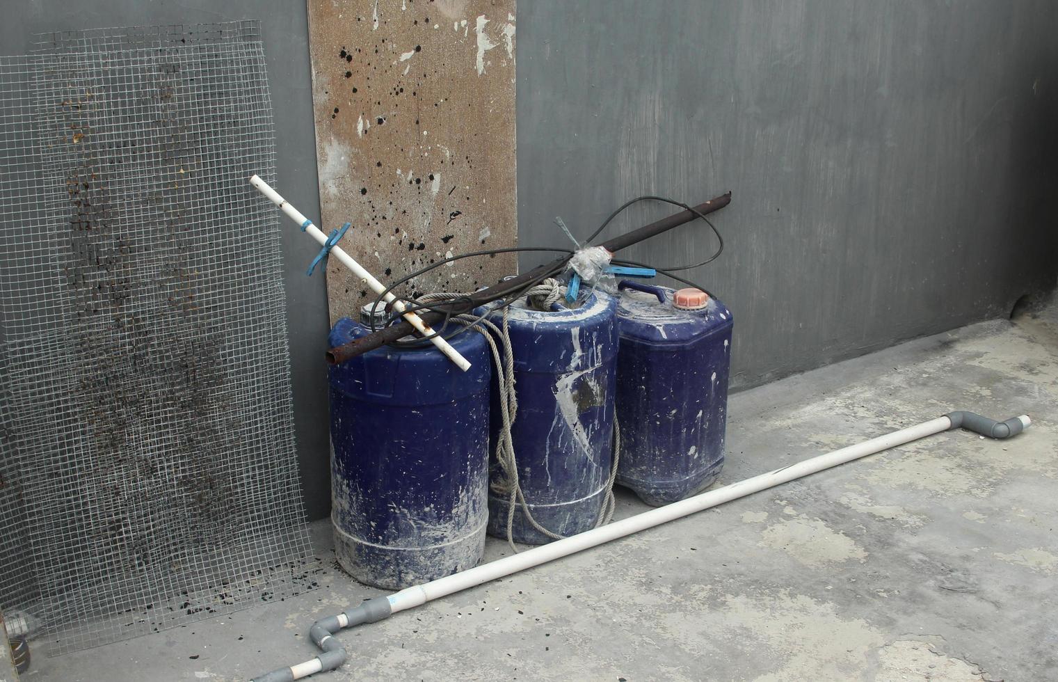 azul plástico pintura água balde em concreto chão e cinzento paredes e madeira prancha ao lado aço rede malha ao lado isto. foto