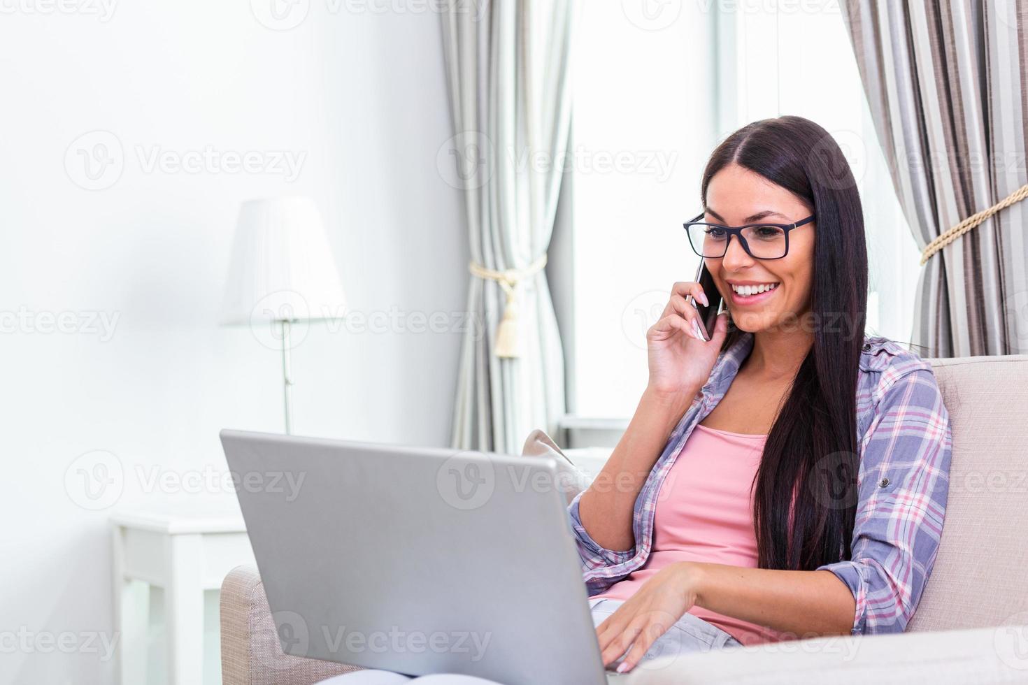 mulher feliz sentada no sofá com o laptop e falando no telefone em casa. jovem empresária de sucesso trabalhando em casa enquanto fala ao telefone. estudante universitário estudando no laptop e usando o telefone. foto