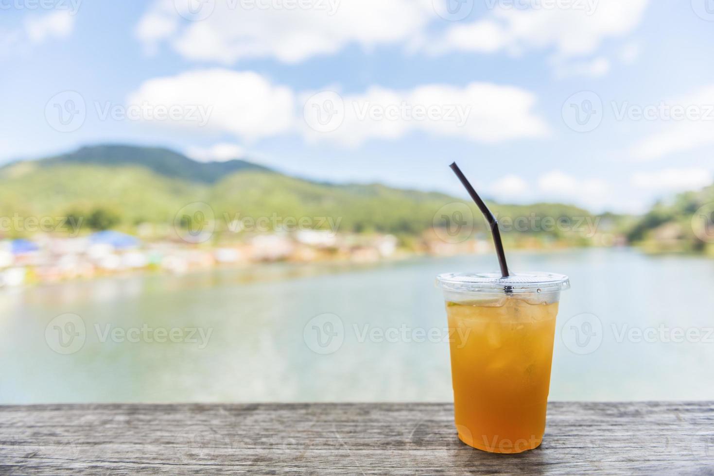 Chá gelado de limão em mesa de madeira com vista para o lago foto