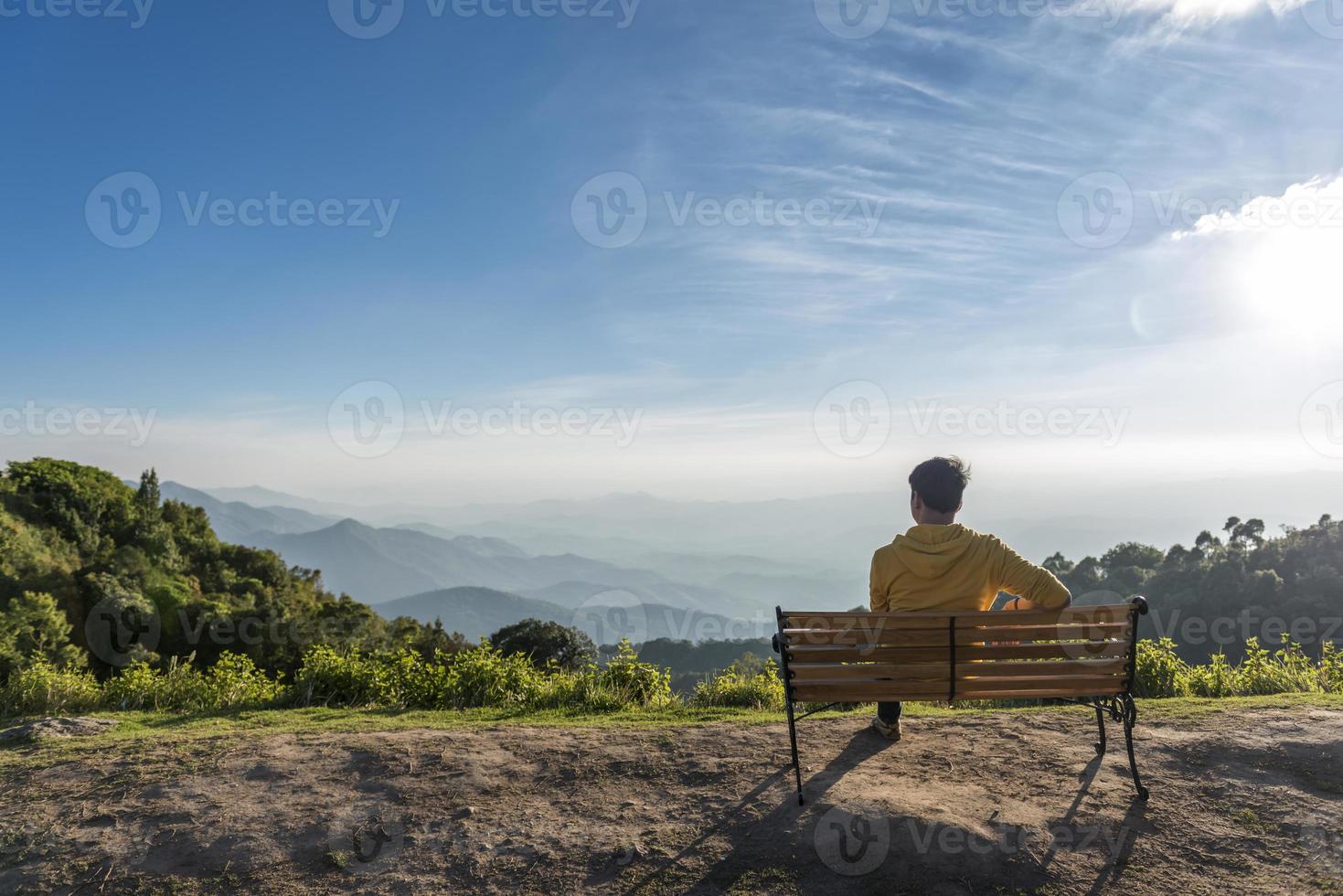 homem viajante sentado em um banco de madeira com montanhas foto