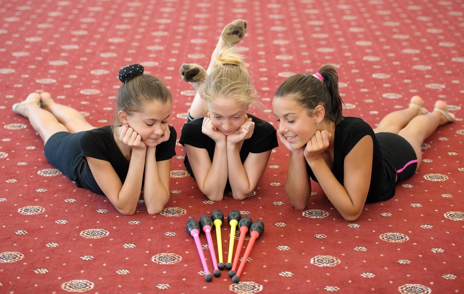 três garotas no chão olhando bastões de ginástica foto