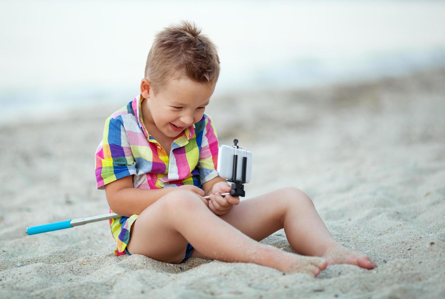 menino com bastão de selfie na praia foto