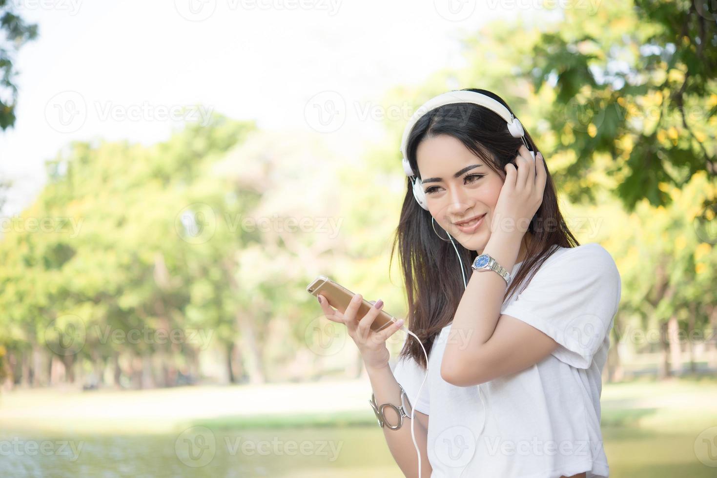 retrato de uma menina sorridente com fones de ouvido ouvindo música na natureza foto