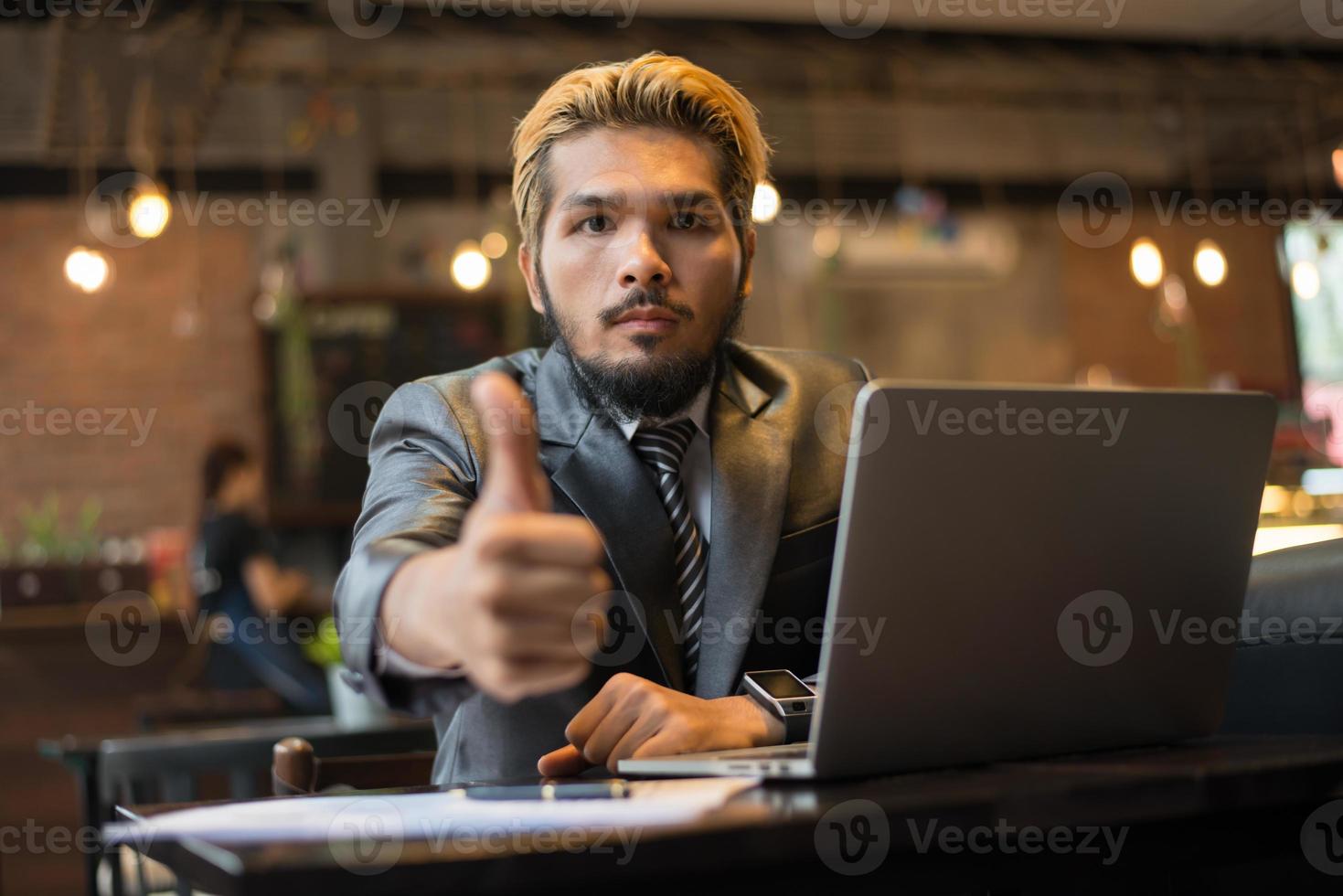 empresário levanta o polegar enquanto trabalha com o laptop na cafeteria foto