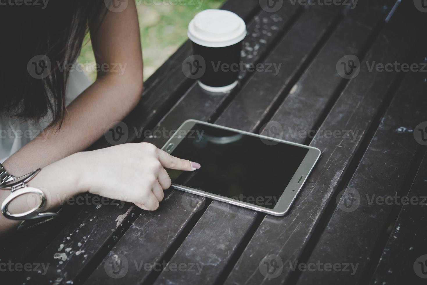 close-up de mulher segurando o computador tablet na mesa de madeira com uma xícara de café foto