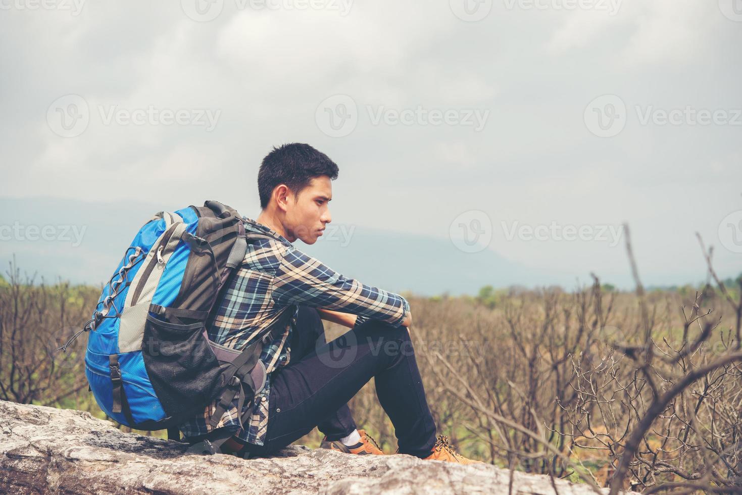 caminhante jovem hippie com mochila sentado no topo da montanha foto