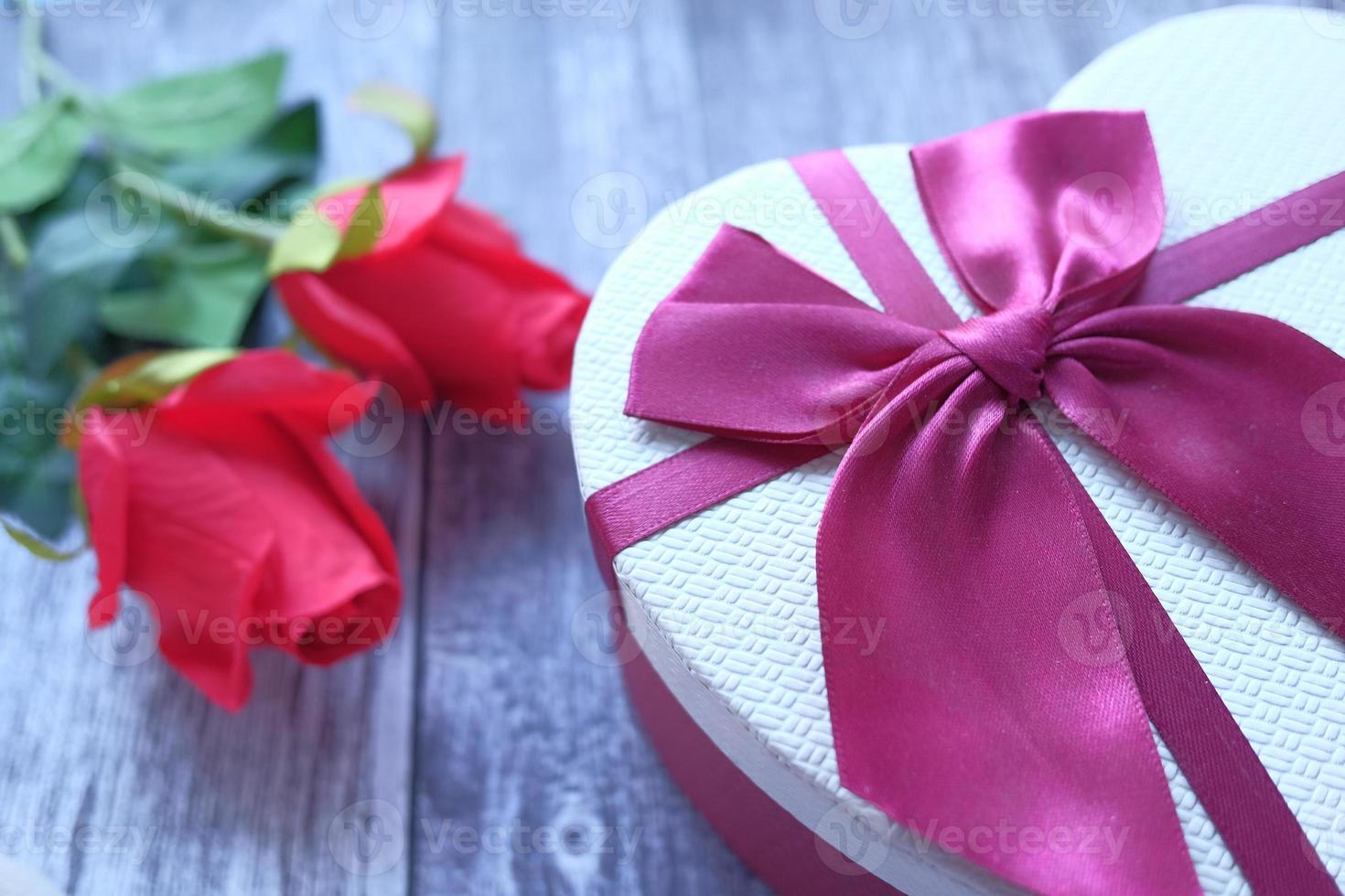 caixa de presente em forma de coração e flor rosa em fundo de madeira foto