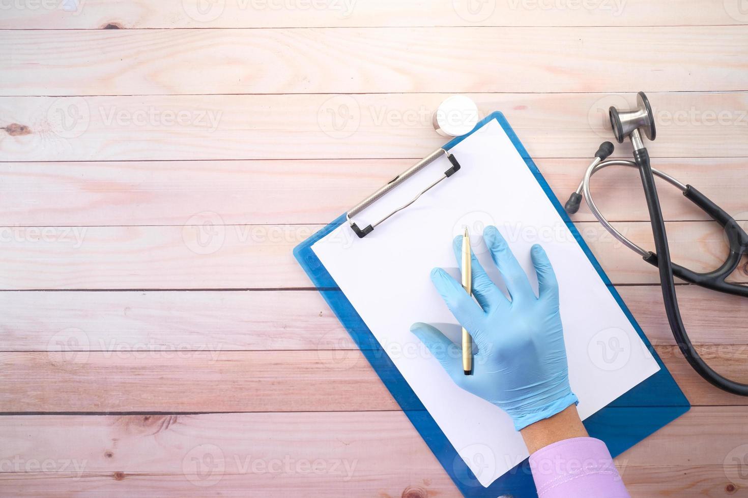 mão do médico em luvas de látex escrevendo a receita na mesa, vista superior foto