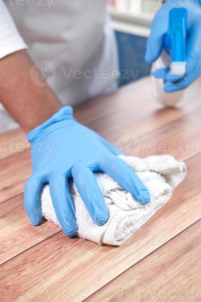 pessoa com luvas descartáveis usando spray desinfetante para limpar a superfície da mesa foto