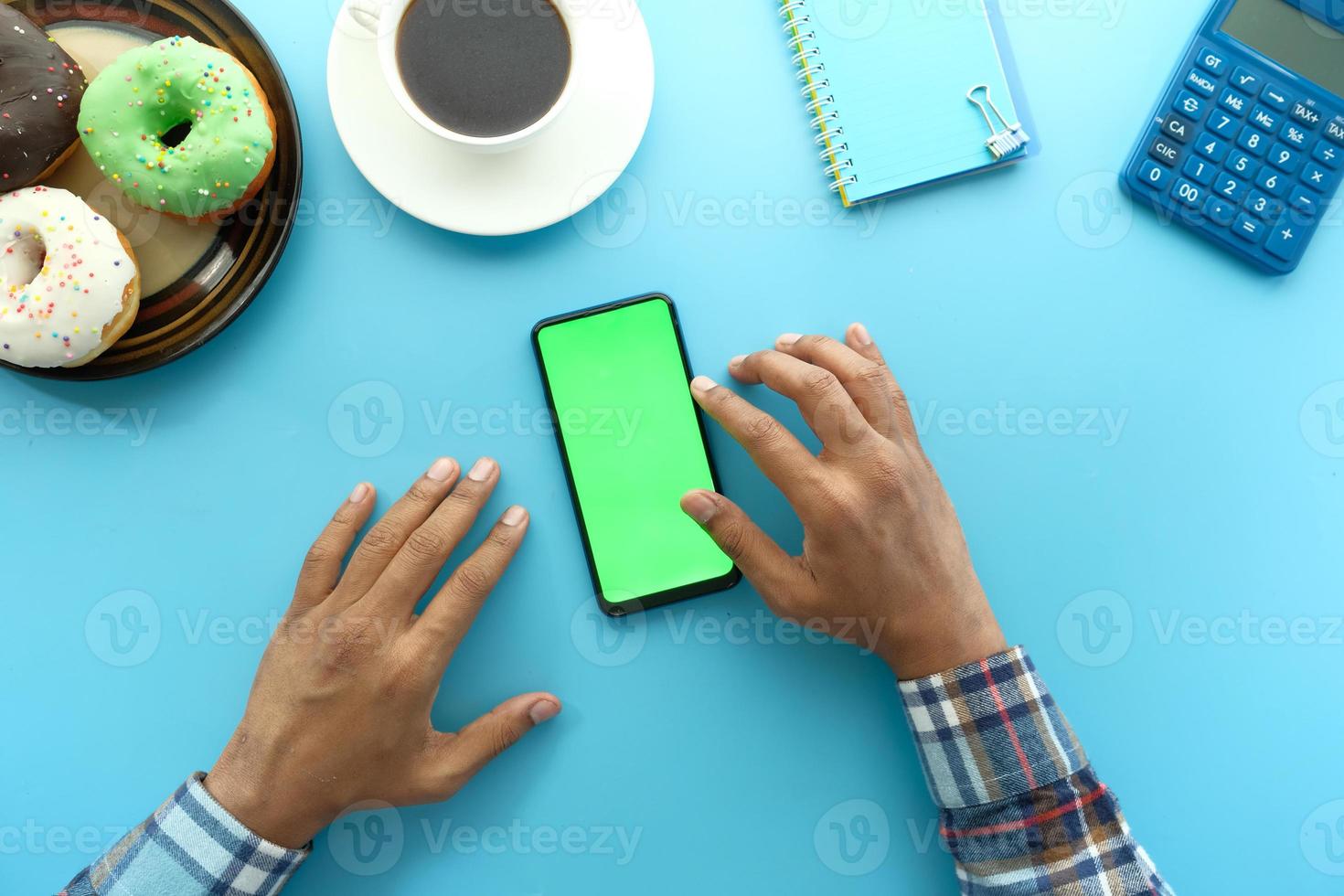 vista superior da mão do homem usando smartphone com donuts e chá no fundo azul foto