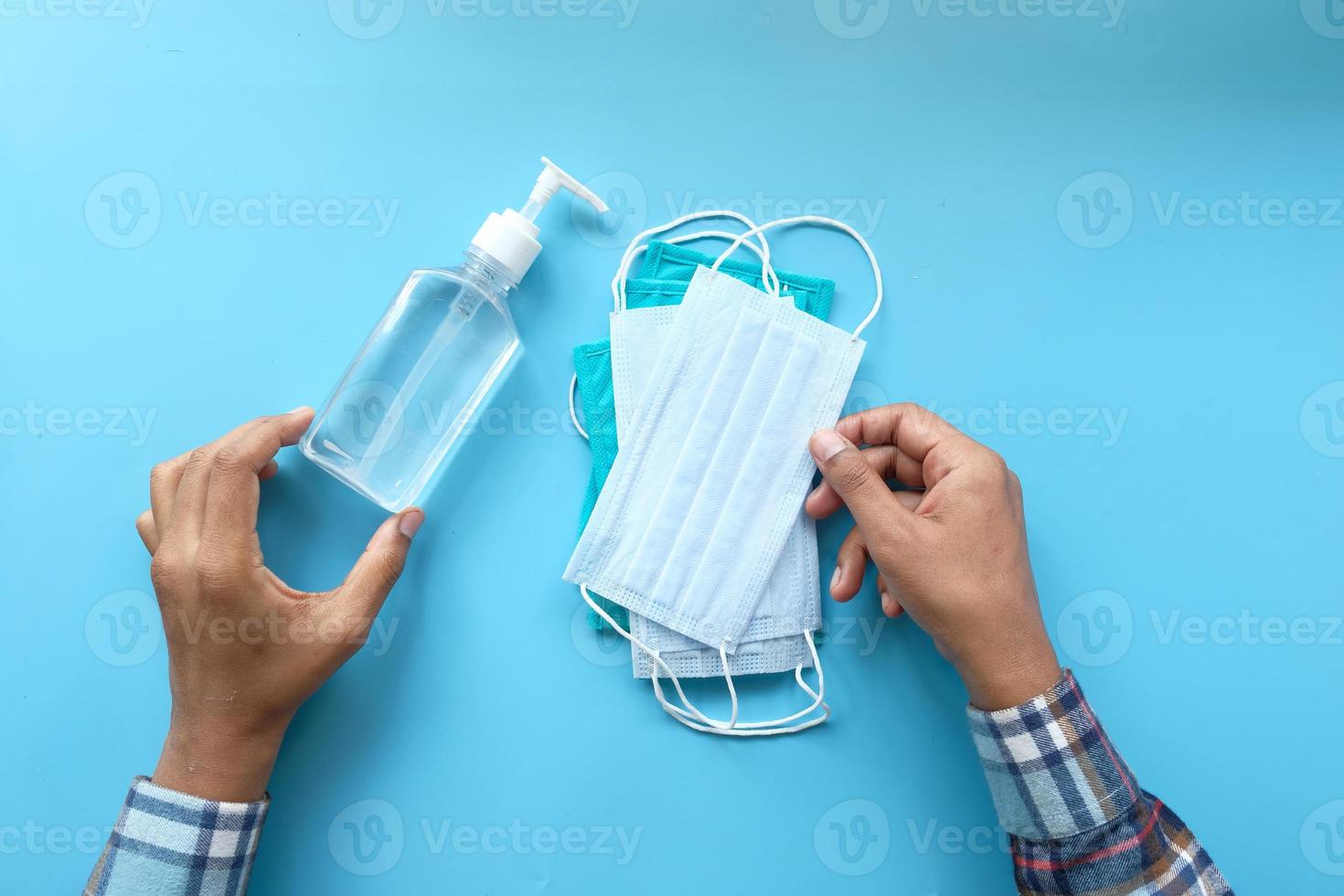 vista superior da mão de um homem segurando máscara cirúrgica e gel desinfetante foto