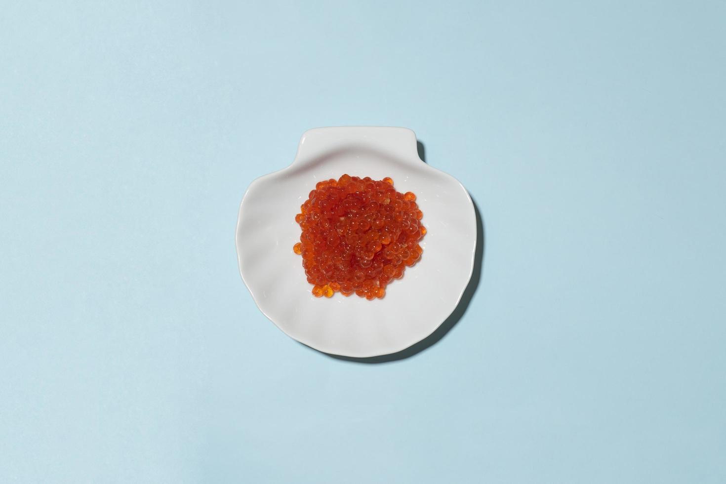caviar vermelho em placa de orcelana branca sobre fundo azul foto