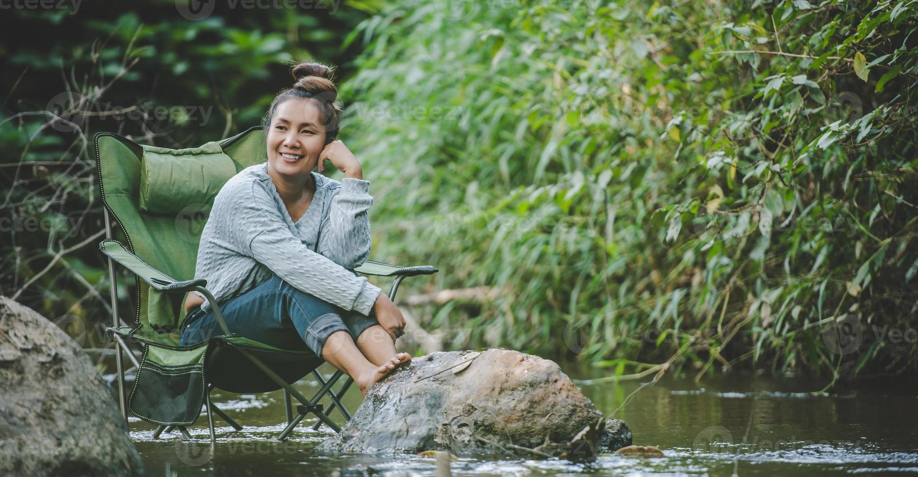 jovem sentada na cadeira de acampamento no riacho para relaxar foto
