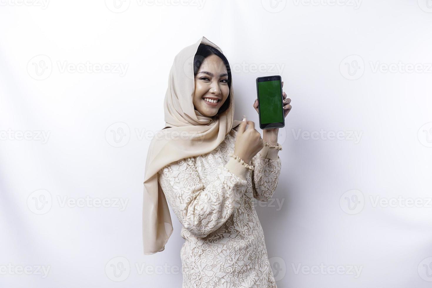 uma retrato do uma feliz ásia muçulmano mulher vestindo uma hijab, mostrando dela telefone tela, isolado de branco fundo foto